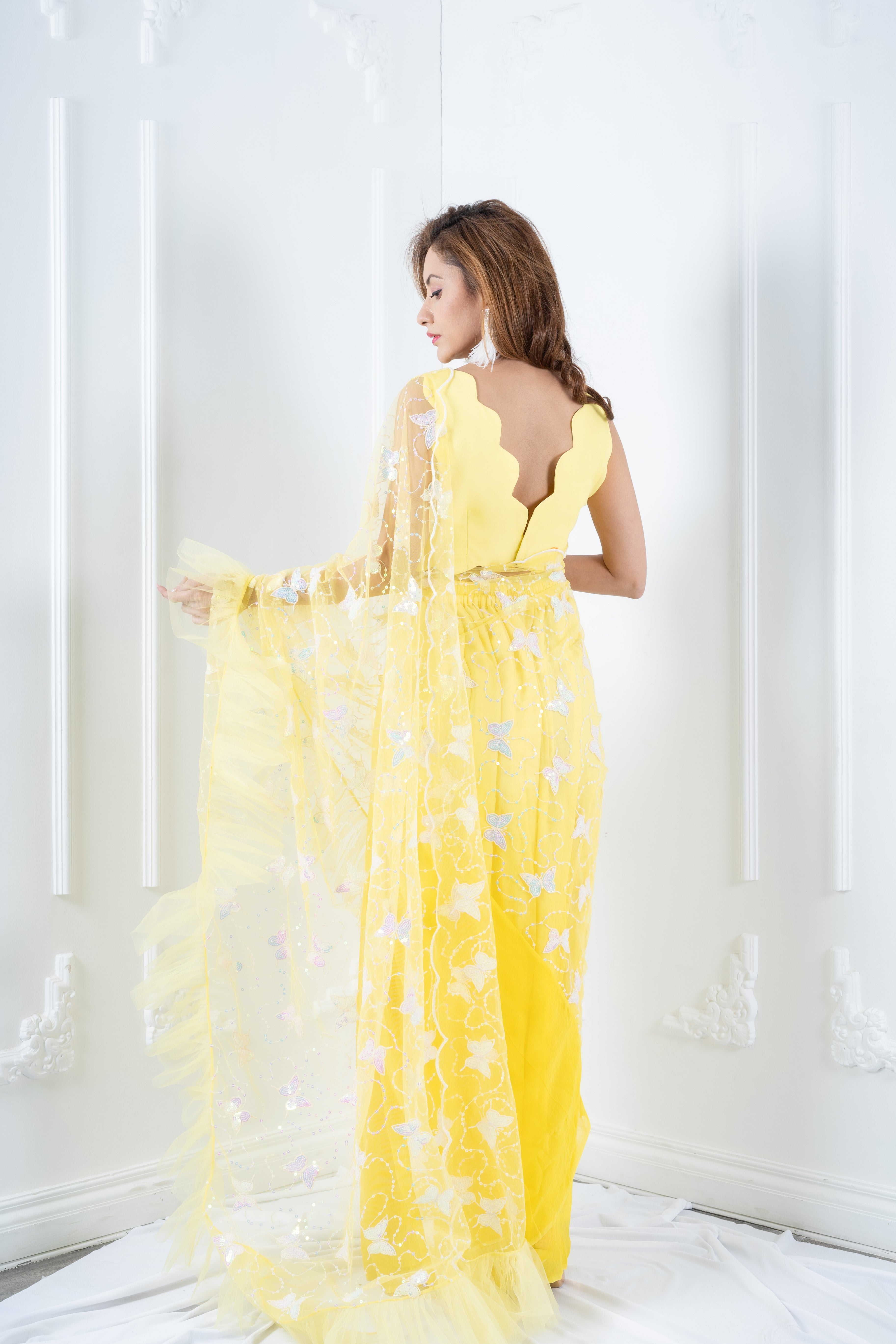 Back view of designer yellow saree showing scalloped blouse and draped pallu.